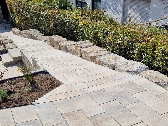 Plattenweg mit Natursteinmauer und gepflegter Hecke